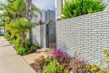 Pathway along wrought iron gate and brick fence at the entrance of modern home