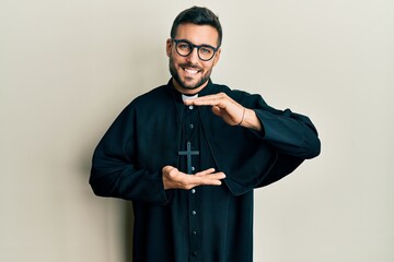 Young hispanic man wearing priest uniform standing over white background gesturing with hands...