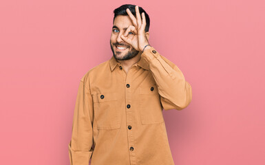 Young hispanic man wearing casual clothes doing ok gesture with hand smiling, eye looking through fingers with happy face.
