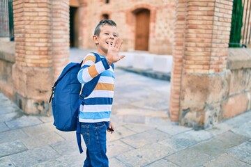 Adorable caucasian student boy smiling happy saying goodbye with hand at the school.