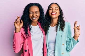 African american mother and daughter wearing business style gesturing finger crossed smiling with...