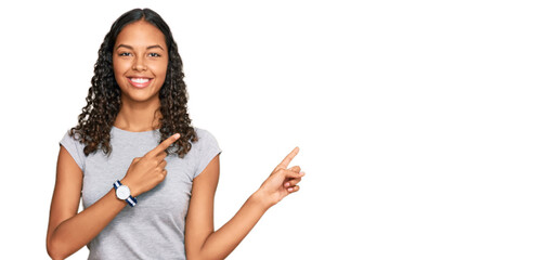 Young african american girl wearing casual clothes smiling and looking at the camera pointing with two hands and fingers to the side.