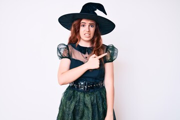 Young beautiful woman wearing witch halloween costume pointing aside worried and nervous with forefinger, concerned and surprised expression