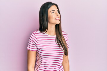 Fototapeta premium Young brunette woman wearing casual clothes over pink background looking away to side with smile on face, natural expression. laughing confident.