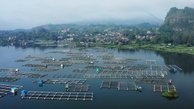 Aerial view of the fish farming aquaculture industry located on the lake of Batur in Bali Indonesia with the mystic volcano Batur standing on the horizon and surrounded with clouds.