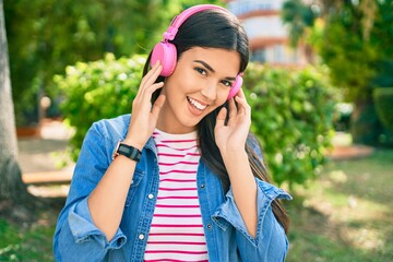 Young beautiful hispanic girl listening to music using headphones standing at the park.