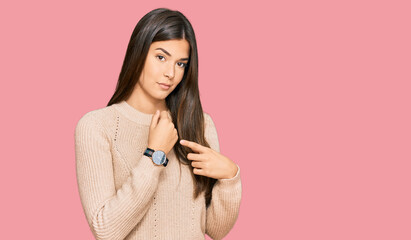 Young brunette woman wearing casual winter sweater in hurry pointing to watch time, impatience,...