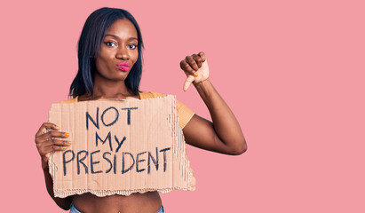 Young african american woman holding not my president protest banner with angry face, negative sign showing dislike with thumbs down, rejection concept