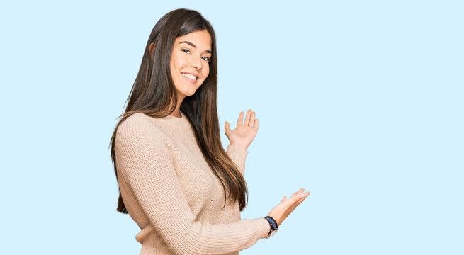 Young brunette woman wearing casual winter sweater inviting to enter smiling natural with open hand