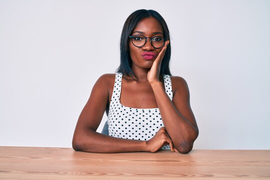 Young african american woman wearing casual clothes and glasses sitting on the table thinking looking tired and bored with depression problems with crossed arms.
