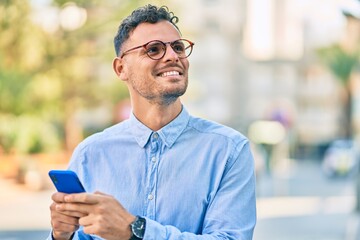 Young hispanic businessman smiling happy using smartphone at the city.