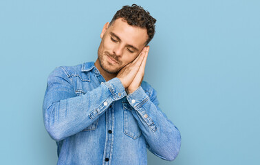 Young hispanic man wearing casual denim jacket sleeping tired dreaming and posing with hands together while smiling with closed eyes.