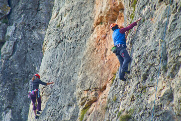 Horizontal photo of two highly equipped climbers climbing a reddish mountain,
