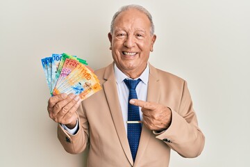 Senior caucasian man holding swiss franc banknotes smiling happy pointing with hand and finger