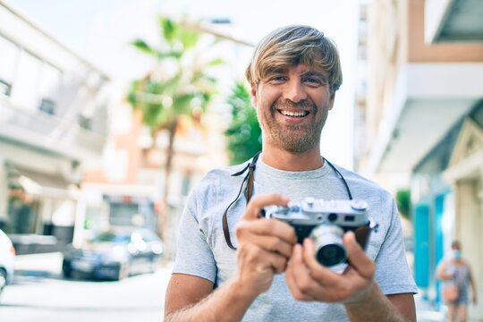 Young irish photographer man smiling happy using vintage camera at street of city.