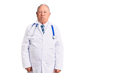 Senior handsome grey-haired man wearing doctor coat and stethoscope puffing cheeks with funny face. mouth inflated with air, crazy expression.