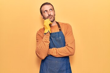 Young handsome man wearing gardener apron and gloves thinking concentrated about doubt with finger...