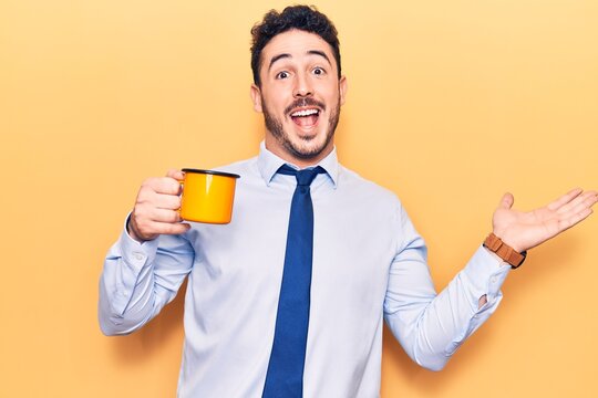 Young hispanic man wearing business clothes holding coffee celebrating achievement with happy smile and winner expression with raised hand