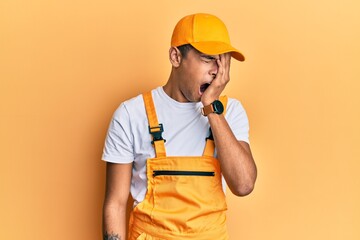 Young handsome african american man wearing handyman uniform over yellow background yawning tired...