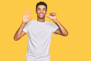 Young handsome african american man wearing casual white tshirt showing and pointing up with fingers number six while smiling confident and happy.