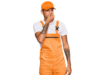 Young handsome african american man wearing handyman uniform smelling something stinky and...