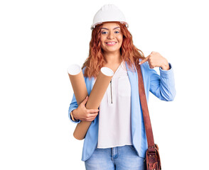 Young latin woman wearing architect hardhat holding blueprints pointing finger to one self smiling happy and proud