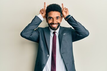 Handsome hispanic man with beard wearing business suit and tie posing funny and crazy with fingers on head as bunny ears, smiling cheerful