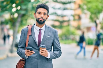 Young african american businessman with serious expression using smartphone and drinking coffee at the city.