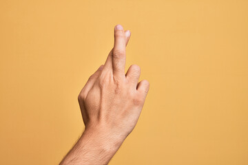 Hand of caucasian young man showing fingers over isolated yellow background gesturing fingers crossed, superstition and lucky gesture, lucky and hope expression