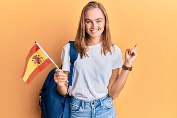 Beautiful blonde woman exchange student holding spanish flag smiling happy pointing with hand and...