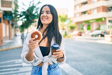Young hispanic girl  having breakfast eating donut and drinking take away coffee at the city.