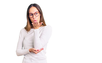 Beautiful brunette young woman wearing casual white sweater and glasses looking at the camera blowing a kiss with hand on air being lovely and sexy. love expression.