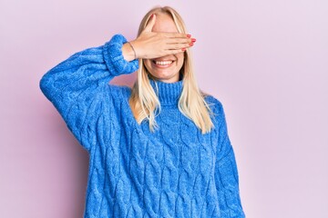 Young blonde girl wearing wool winter sweater smiling and laughing with hand on face covering eyes for surprise. blind concept.