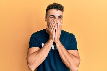 Hispanic young man wearing volunteer t shirt laughing and embarrassed giggle covering mouth with hands, gossip and scandal concept