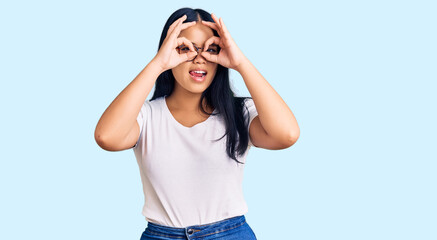 Young beautiful asian girl wearing casual clothes and glasses doing ok gesture like binoculars sticking tongue out, eyes looking through fingers. crazy expression.