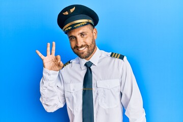 Handsome man with beard wearing airplane pilot uniform smiling positive doing ok sign with hand and fingers. successful expression.