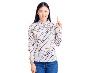 Young beautiful chinese woman wearing casual shirt showing and pointing up with finger number one while smiling confident and happy.