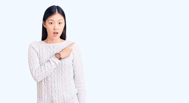 Young beautiful chinese woman wearing casual sweater surprised pointing with finger to the side, open mouth amazed expression.