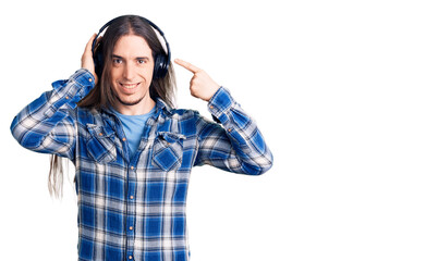 Obraz na płótnie Canvas Young adult man with long hair listening to music using headphones smiling happy pointing with hand and finger