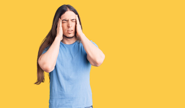 Young adult man with long hair wearing casual clothes suffering from headache desperate and stressed because pain and migraine. hands on head.