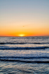 Ocean and waves with orange sun in the horizon in San Diego California at sunset