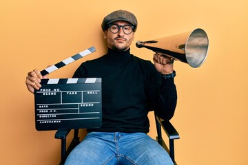 Handsome man with tattoos holding video film clapboard and louder relaxed with serious expression...