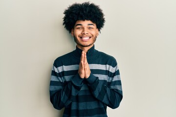 Fototapeta na wymiar Young african american man with afro hair wearing casual clothes praying with hands together asking for forgiveness smiling confident.