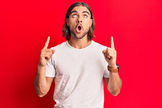 Young handsome man wearing casual clothes amazed and surprised looking up and pointing with fingers and raised arms.