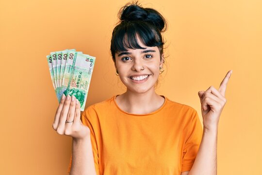 Young hispanic girl holding 50 hong kong dollars banknotes smiling happy pointing with hand and finger to the side