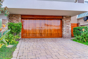 House garage with shiny brown wooden door against stone brick wall and gate