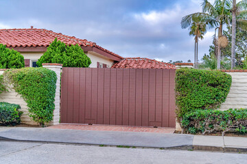 Brown gate and white brick fence against red tile roof of house in San Diego CA