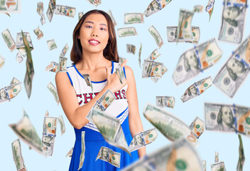 Young beautiful chinese girl wearing cheerleader uniform cheerful with a smile on face pointing...