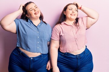 Young plus size twins wearing casual clothes smiling confident touching hair with hand up gesture, posing attractive and fashionable