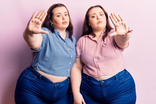 Young plus size twins wearing casual clothes doing frame using hands palms and fingers, camera perspective